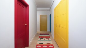 A narrow hallway with a red door on the left, a yellow door on the right, and a beige door at the end. - Metro Młynów Colourful Apartment (Warszawa)