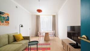 A modern living room with a green sofa, a small table, a TV, and a colorful rug. - Metro Młynów Colourful Apartment (Warszawa)