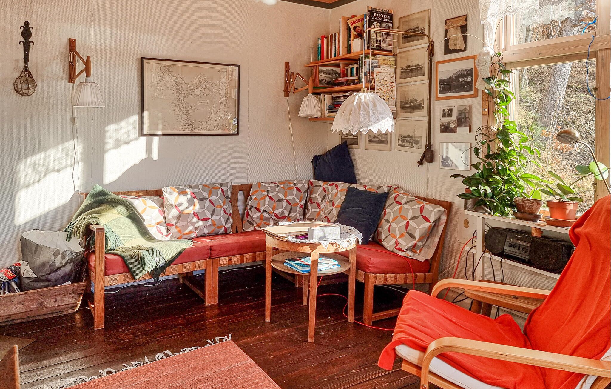 Un salón acogedor con un sofá de madera, un sillón rojo y una pequeña mesa. Hay estanterías llenas de libros y un mapa en la pared.