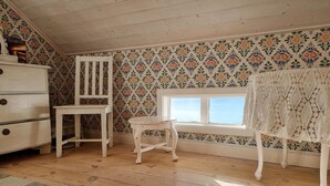 A room with wooden flooring, a white dresser, two white chairs, a window with a view, and floral wallpaper. - Nice home in Nösund with house sea view (Nösund)