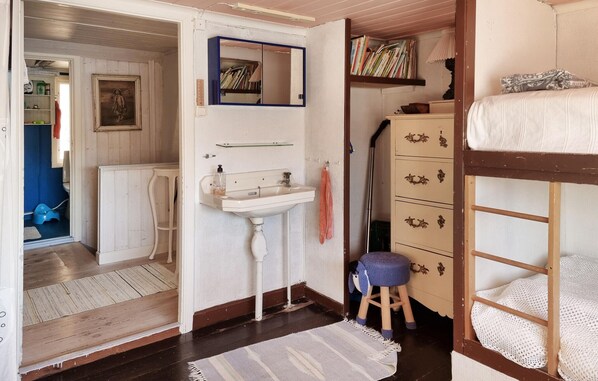A room with a bunk bed, a small stool, a sink, a mirror, and a bookshelf.