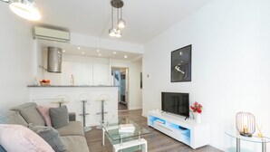 Un soggiorno moderno con un tavolino in vetro, un divano grigio e una TV su un mobile bianco.