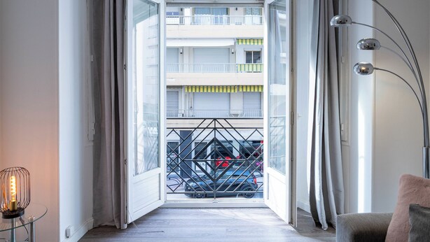 Vista attraverso una porta aperta su un balcone con cancello in metallo, un'auto parcheggiata all'esterno e una lampada da terra moderna.