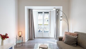 Un soggiorno moderno con un tavolino in vetro, un divano, una lampada da terra e vista su un balcone con ringhiera.