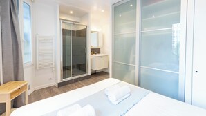 Una moderna camera d'hotel con un letto grande, un armadio a muro, un bagno con doccia in vetro e una piccola scrivania.