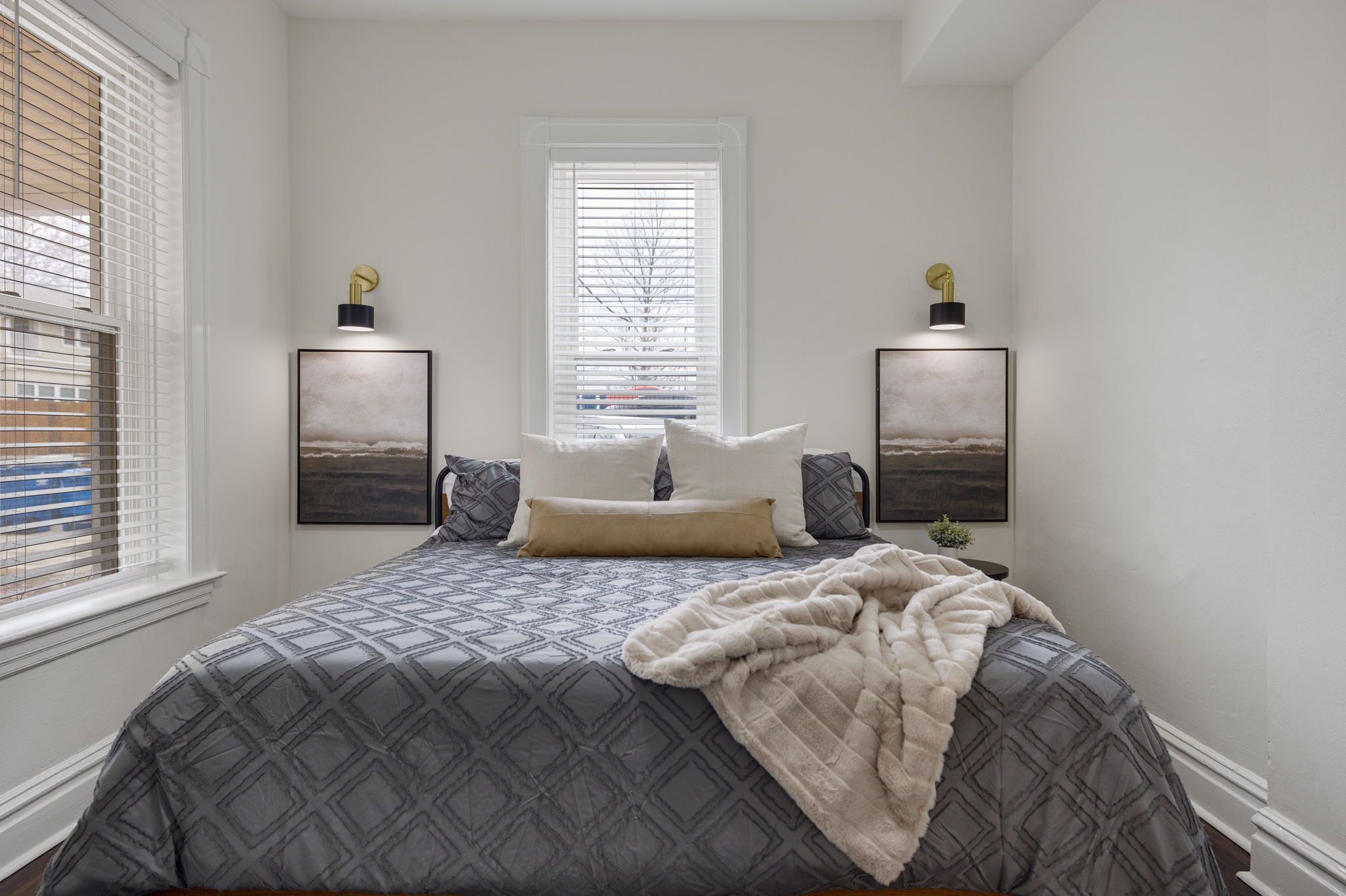 A bedroom with a bed, two wall-mounted lamps, and a window with blinds.
