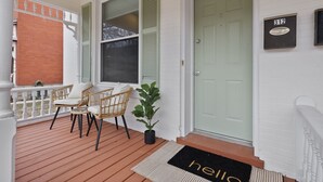 A porch with a wooden deck, wicker chairs, a small potted plant, and a door with a number plaque. - 3BR Historic St. Charles, MO-Walking distance to Main Street (Saint Charles)