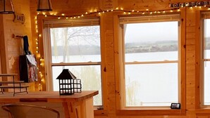 A cabin interior with wooden walls, a bar area, and large windows overlooking a lake.