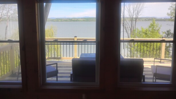 A room with large windows overlooking a lake, a wooden deck with outdoor furniture, and a sign reading 'A Day at the Cabin'.