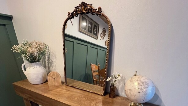A wooden bench with a large mirror, a white vase with flowers, a small wooden sculpture, and a globe. - Cozy Home on the edge of Rolla! (Rolla)