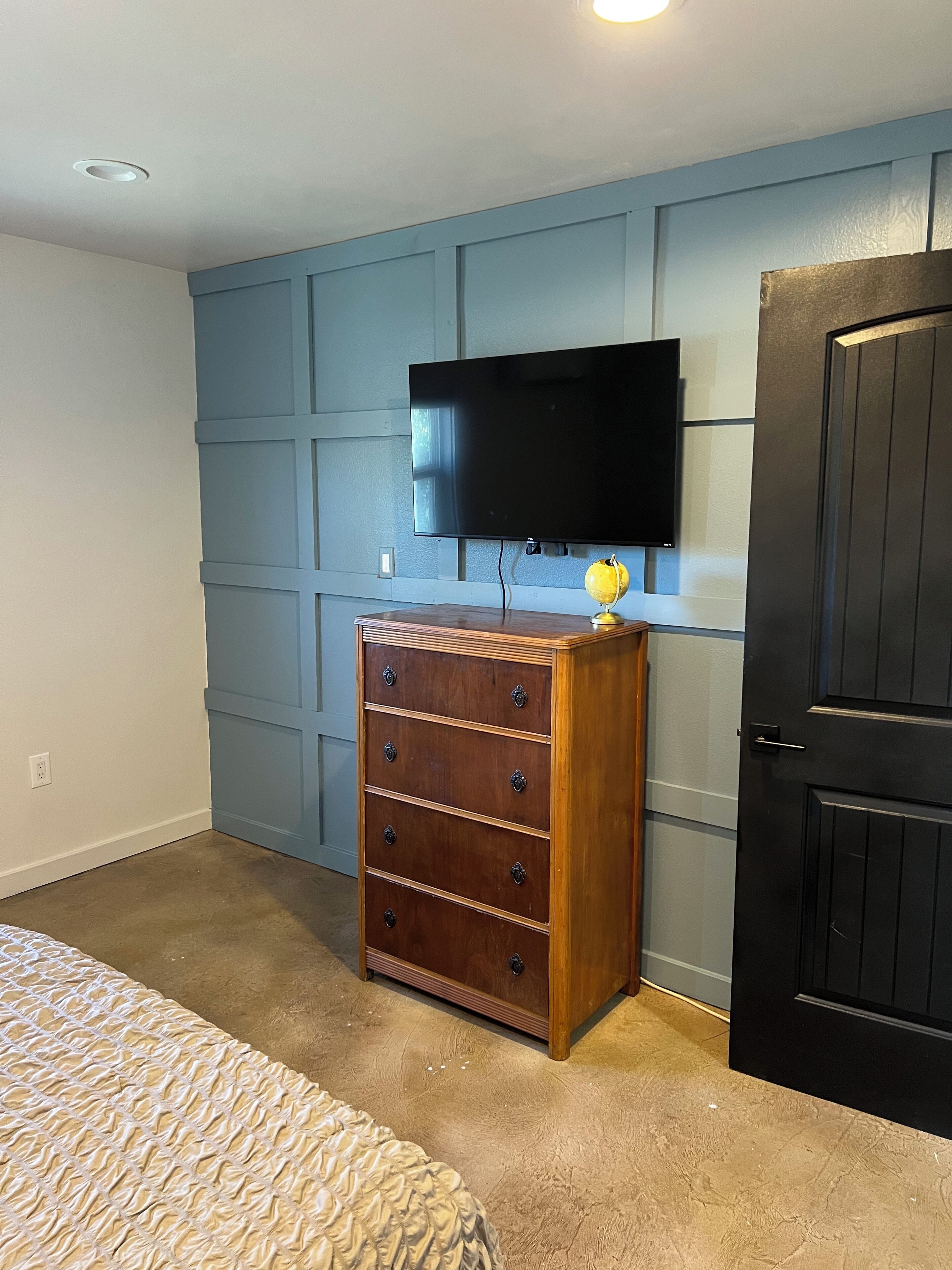 A bedroom with a bed, a dresser, a television mounted on the wall, and a door.