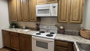 A kitchen with wooden cabinets, a white stove, a microwave, granite countertops, and a small rug. - Cozy Home on the edge of Rolla! (Rolla)