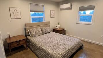 Un dormitorio con una cama grande, dos mesitas de noche, una ventana y un equipo de aire acondicionado.
