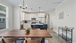 A modern kitchen with white cabinets, stainless steel appliances, and a wooden dining table with chairs. - Entire Cozy Duplex Ideal for Families & Groups (Memphis)