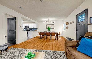 A modern living room with a dining area, wooden flooring, and a kitchen in the background.