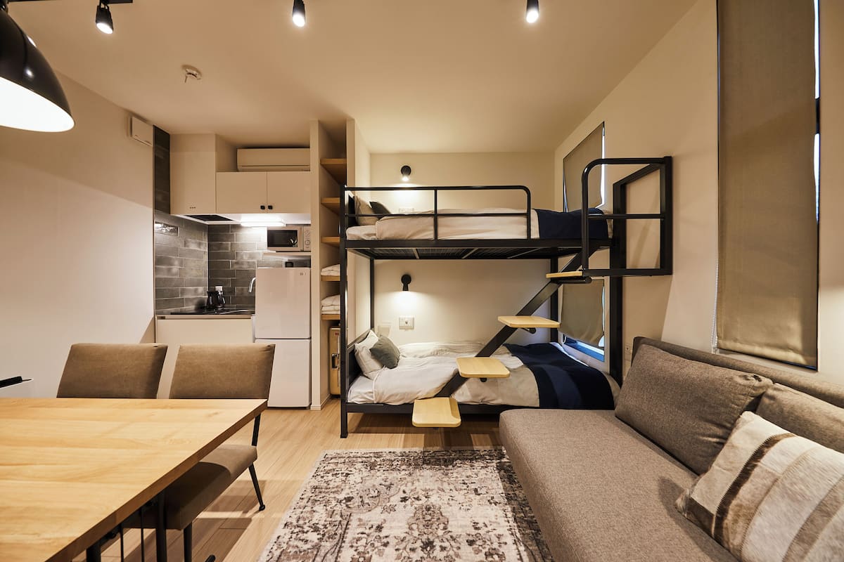 A compact, modern room with a bunk bed, a sofa, a dining table, and a kitchenette.