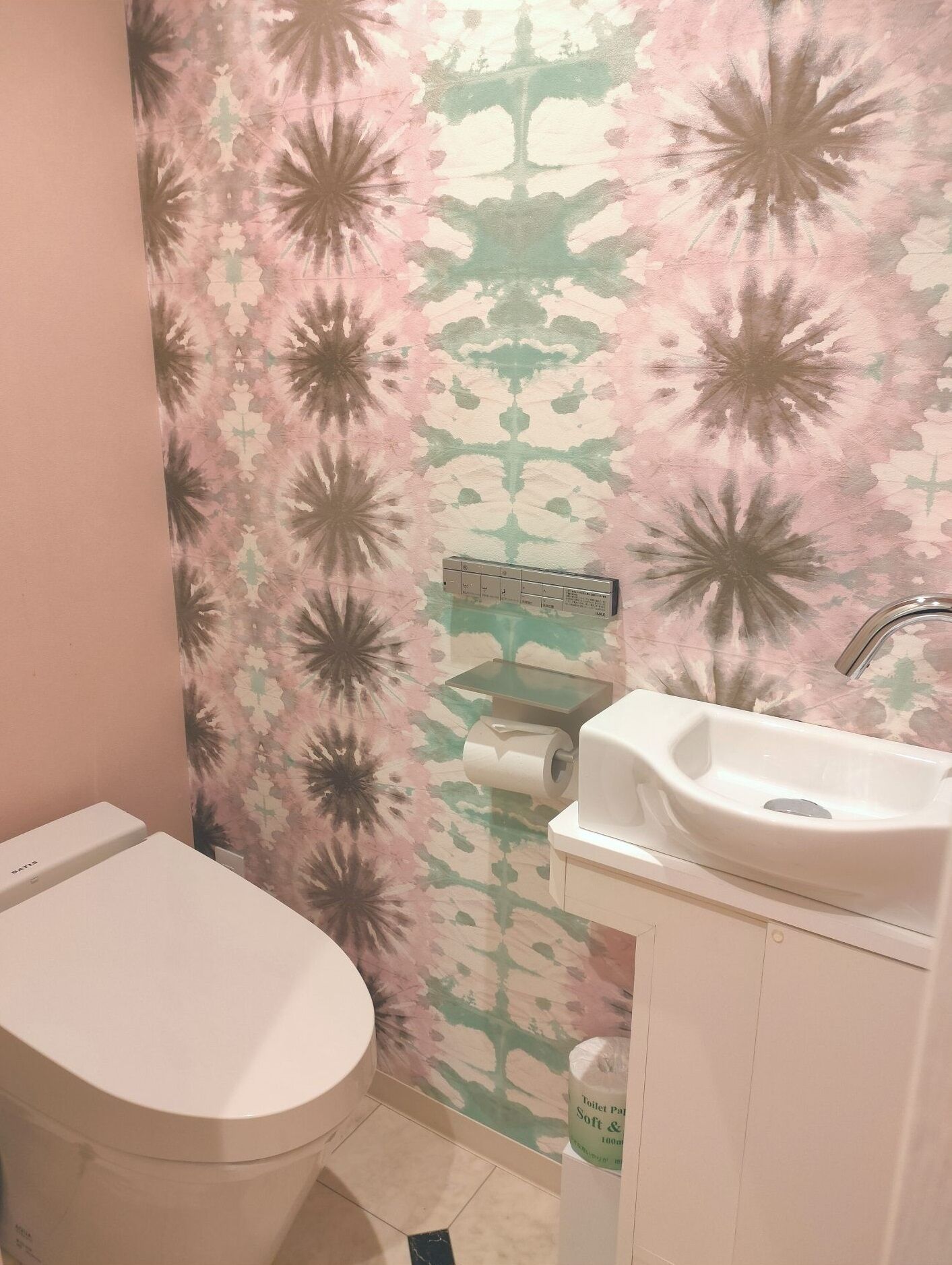 A bathroom with a toilet, sink, and a toilet paper holder.