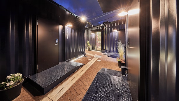 A modern hotel entrance with a dark facade, a welcoming entrance, and a pathway leading to the reception area. - TORACO konohana (Osaka)