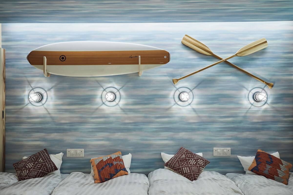 A room with a bed, pillows, a wall-mounted surfboard, and two wooden paddles.