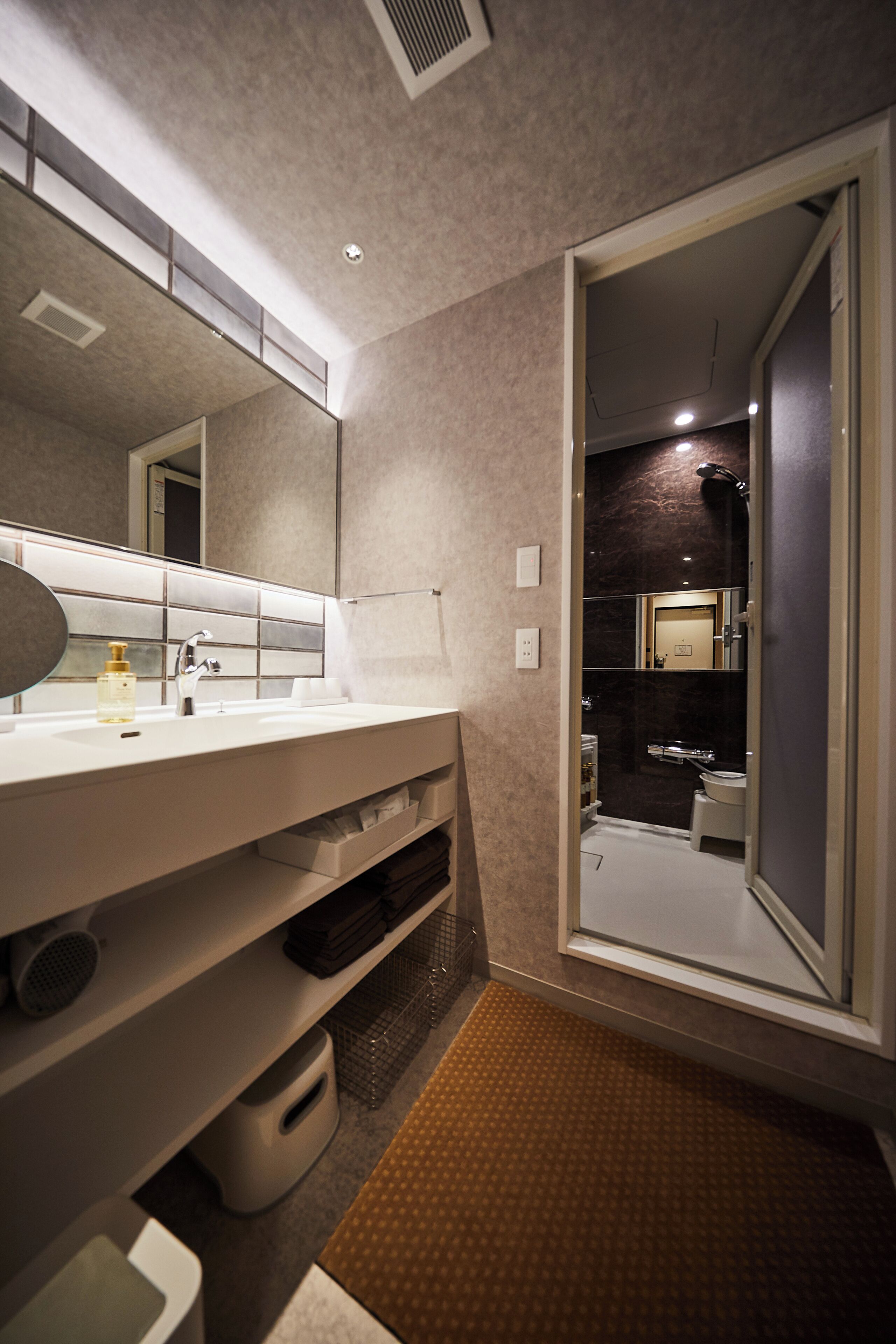 A modern bathroom with a large mirror, white sink, and a shower area.
