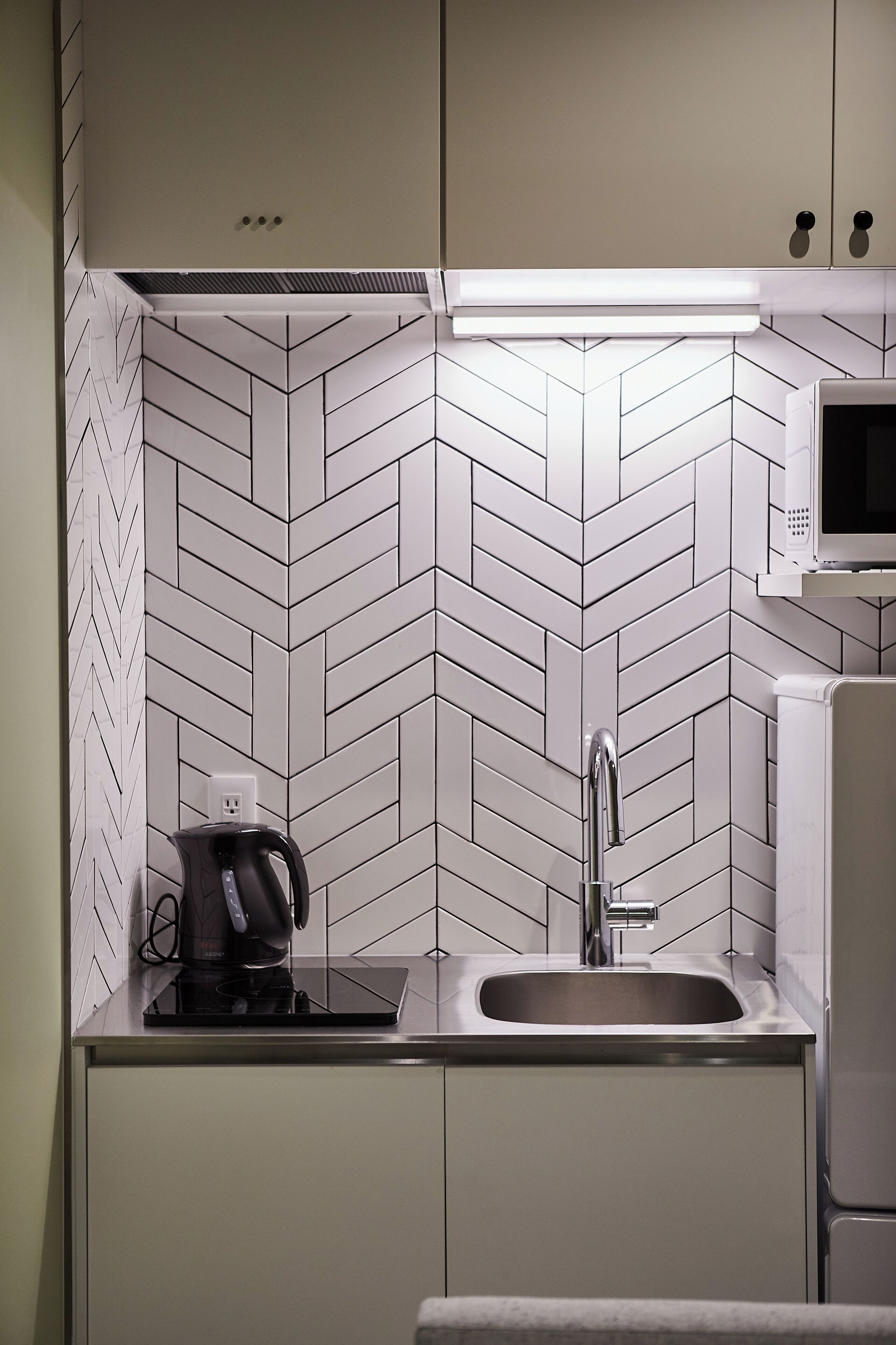 Een moderne keuken met een backsplash van visgraat tegels, een ingebouwde magnetron, een roestvrijstalen spoelbak en een koffiezetapparaat.