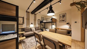 A compact, modern living space with a bunk bed, a sofa, a dining table, and a TV. - TORACO konohana (Osaka)