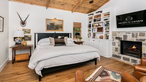 A spacious bedroom with a large bed, a stone fireplace, and a bookshelf filled with books and decorative items.