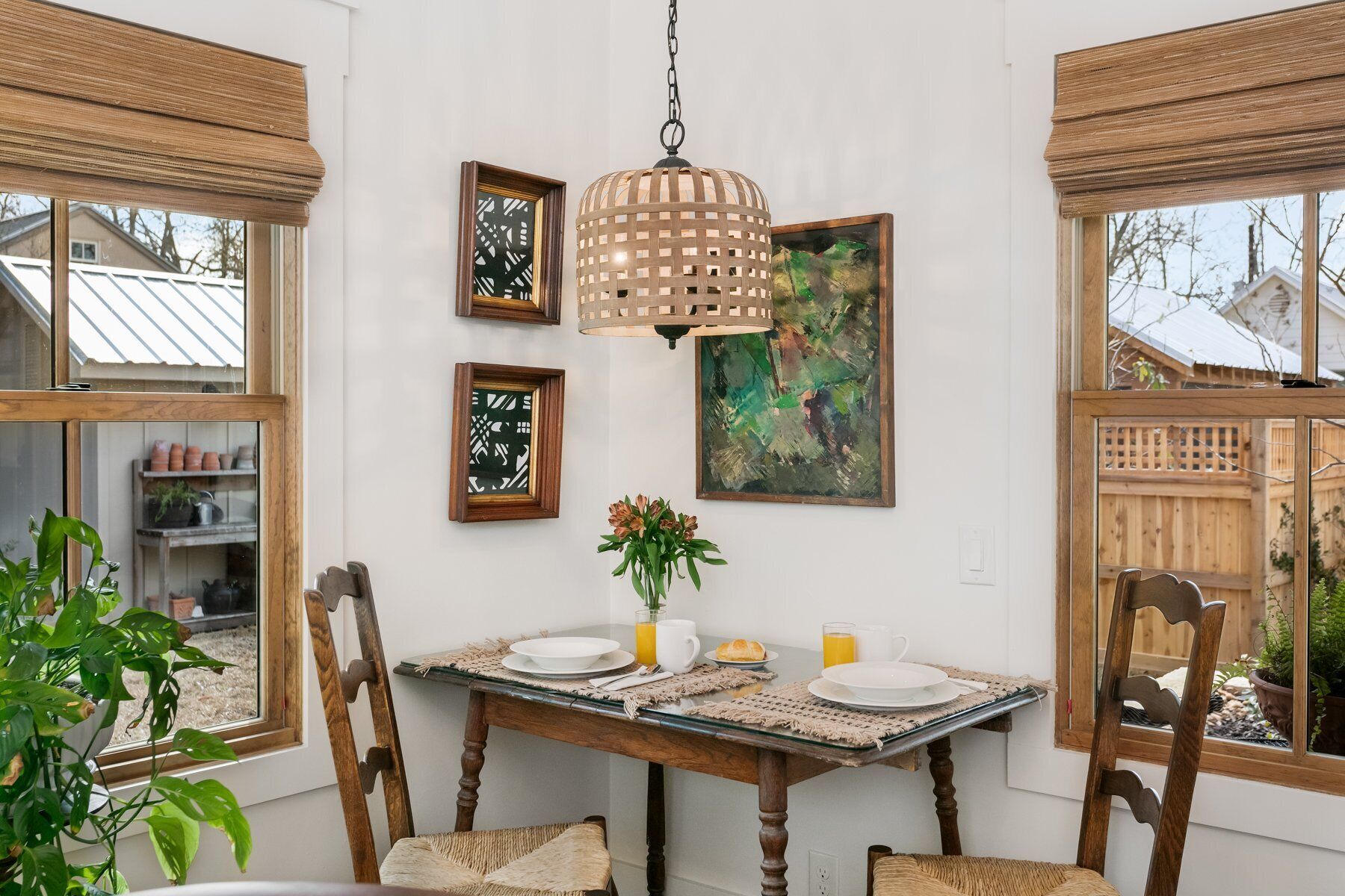 A dining area with a wooden table set for four, surrounded by chairs. There is a hanging light fixture above the table, and artwork is displayed on the walls.