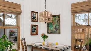 A dining area with a wooden table set for four, surrounded by chairs. There is a hanging light fixture above the table, and artwork is displayed on the walls.