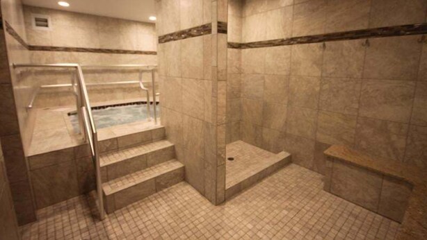Ein Wellnessbereich mit Whirlpool, gefliesten Wänden und einer Treppe zu einem Duschbereich.
