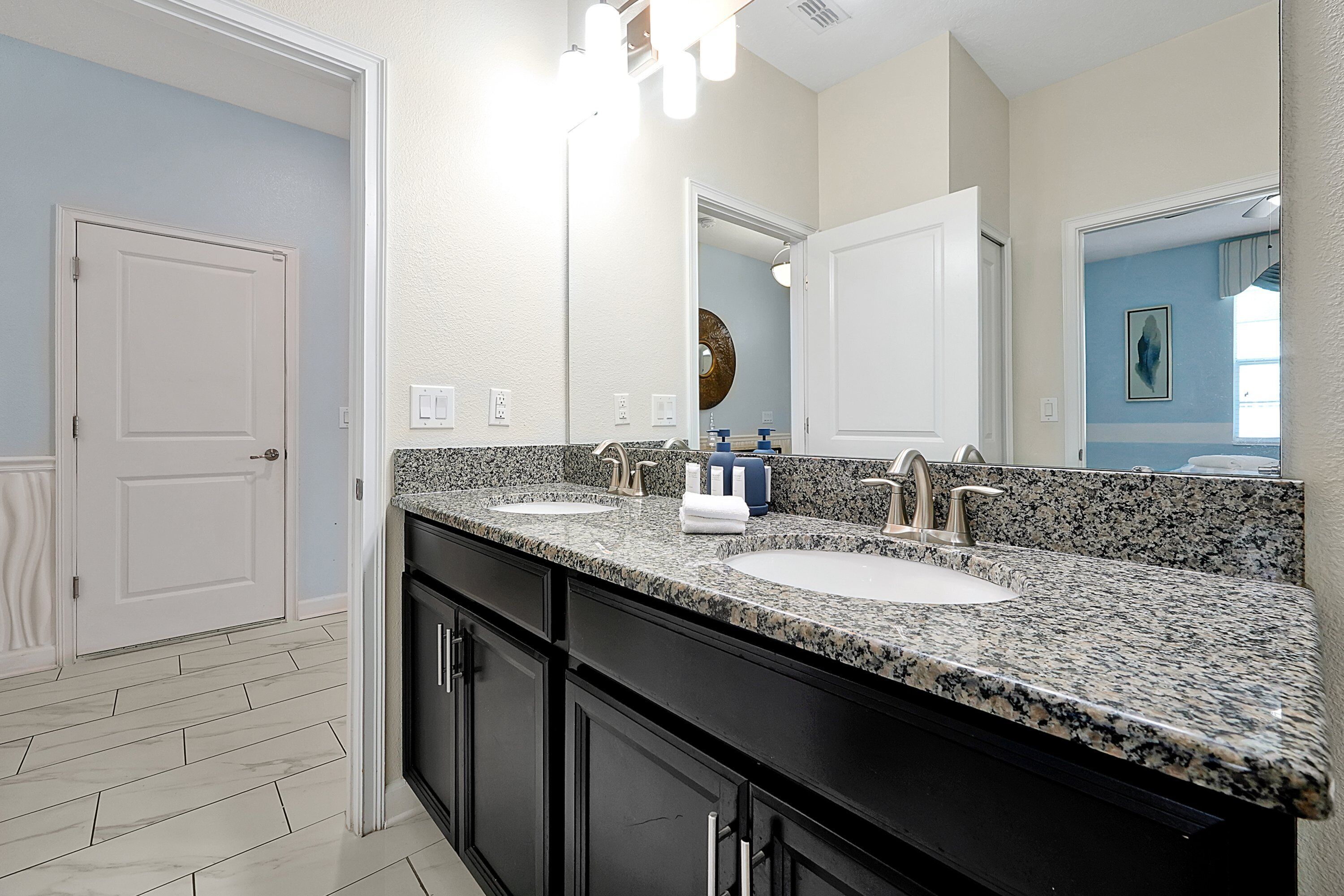 A bathroom with two sinks, a large mirror, and a door leading to another room.