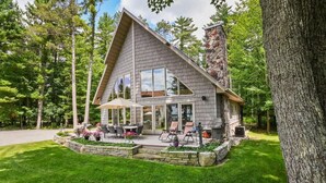 Una casa moderna con chimenea de piedra, un patio con mobiliario exterior y un césped bien cuidado.
