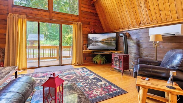Interior acogedor de una cabaña con un ventanal grande, paredes de madera, un televisor, un sofá de cuero y un farol rojo.