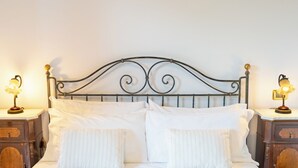 Een net opgemaakt bed met witte lakens en twee kussens, aan weerszijden van houten nachtkastjes met lampen.