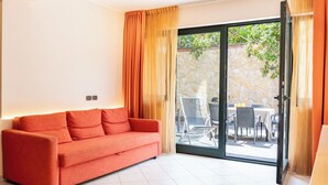A modern living room with a red sofa, a glass door leading to an outdoor patio with a table and chairs. - Etna, Mare e Verde - Open Space (Mascali)