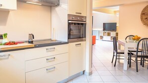 A modern kitchen with a built-in oven, a dining area with a table and chairs, and a television in the background. - Etna, Mare e Verde - Open Space (Mascali)