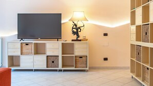 A modern living room with a flat-screen TV, a lamp, and a cabinet with baskets. - Etna, Mare e Verde - Open Space (Mascali)