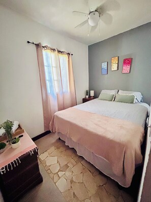 A bedroom with a bed, a nightstand, a potted plant, and a ceiling fan.