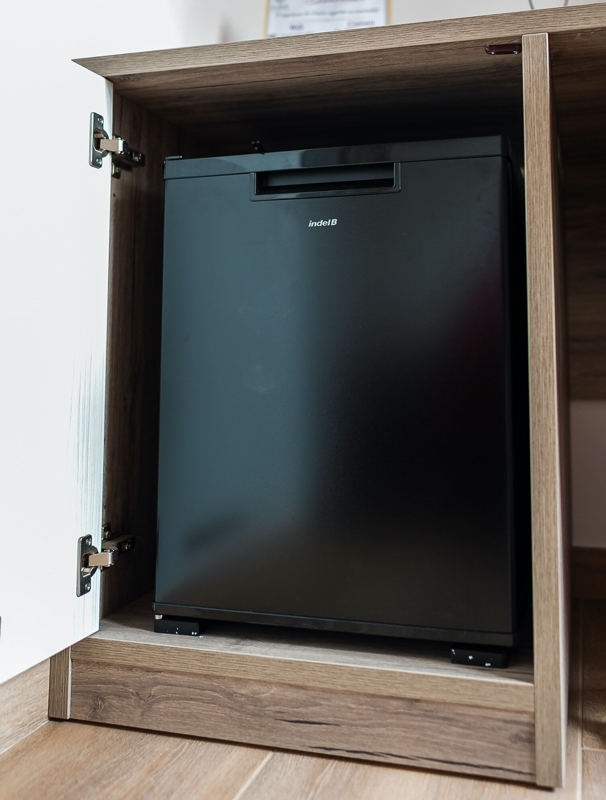 Un refrigerador pequeño y de color oscuro dentro de un gabinete de madera con puerta batiente.