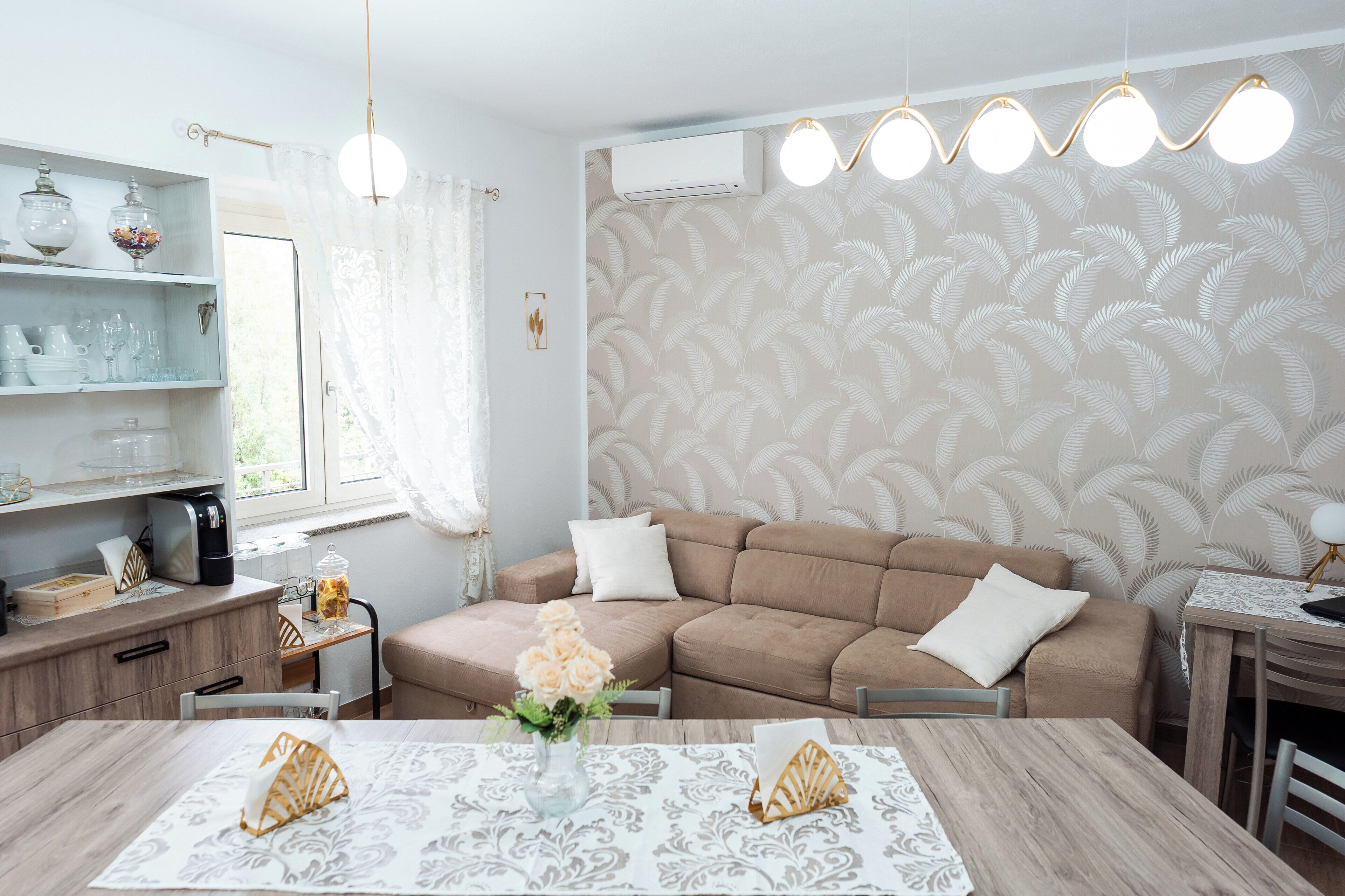 Een moderne woonkamer met een hoekbank, een eettafel met een bloemenvaas, en een keuken met een koffiezetapparaat.