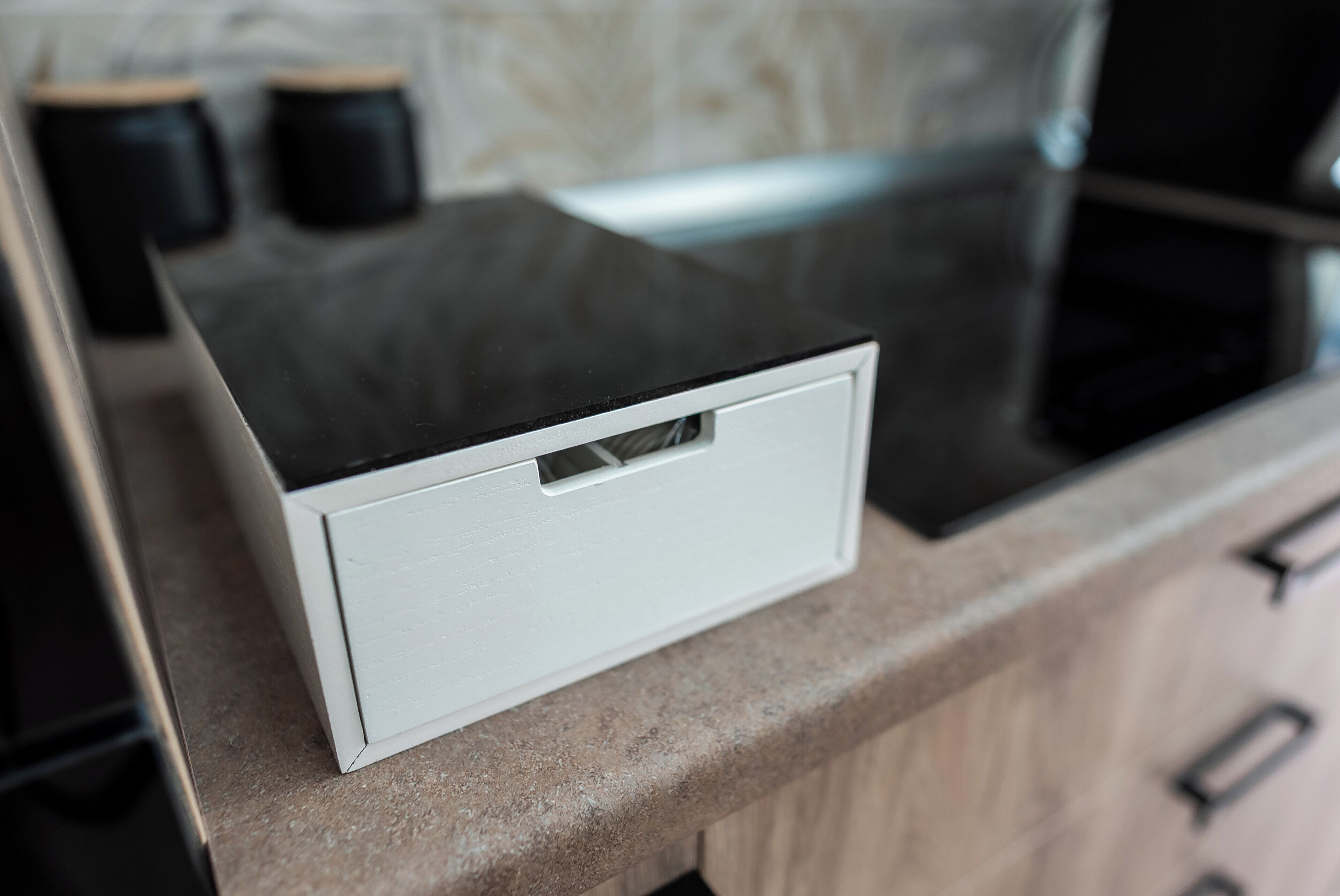Un comptoir de cuisine avec un appareil électroménager blanc, une plaque de cuisson noire et des armoires en bois.