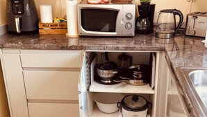 Una cocina con microondas, cafetera, tostadora y un armario oculto con ollas y una cocedora de arroz.