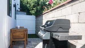 A backyard with a barbecue grill, a wooden chair, and a white fence.