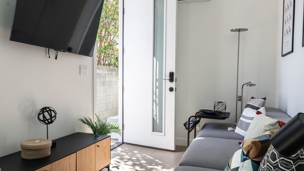 A modern living room with a grey sofa, a black TV mounted on the wall, a wooden cabinet, and a small side table with a plant.
