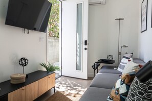 Una sala de estar moderna con un sofá gris, un televisor negro montado en la pared, un mueble de madera y una pequeña mesita con una planta.