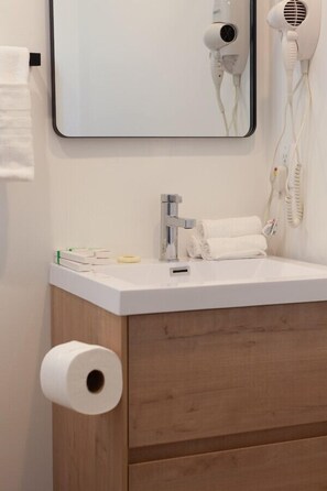 A bathroom with a white sink, a mirror, a hairdryer, and a toilet paper holder. - Built 2024 Scandinavian-Style 1BR/Studio w/ PRIVATE ROOFTOP DECK 360° VIEWS p82 (Los Angeles)