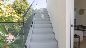 A modern staircase with glass railings leading to a room with a clock on the wall.