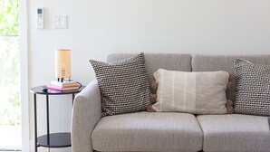 A living room with a sofa, patterned cushions, a small table with a lamp, and a book.