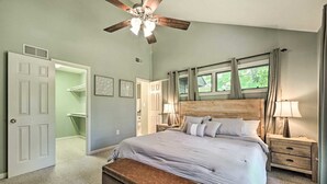 Quarto com uma cama grande, cabeceira de madeira, duas mesas de cabeceira com luminárias, um ventilador de teto e uma janela com cortinas.