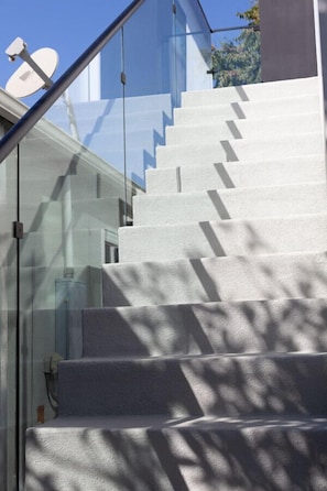 A modern staircase with glass railings and a clear view of the sky.